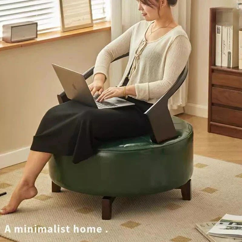 "Person using a laptop on a green chair in a minimalistic home setting."