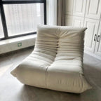 "White lounge chair in a room with large windows and white cabinets."