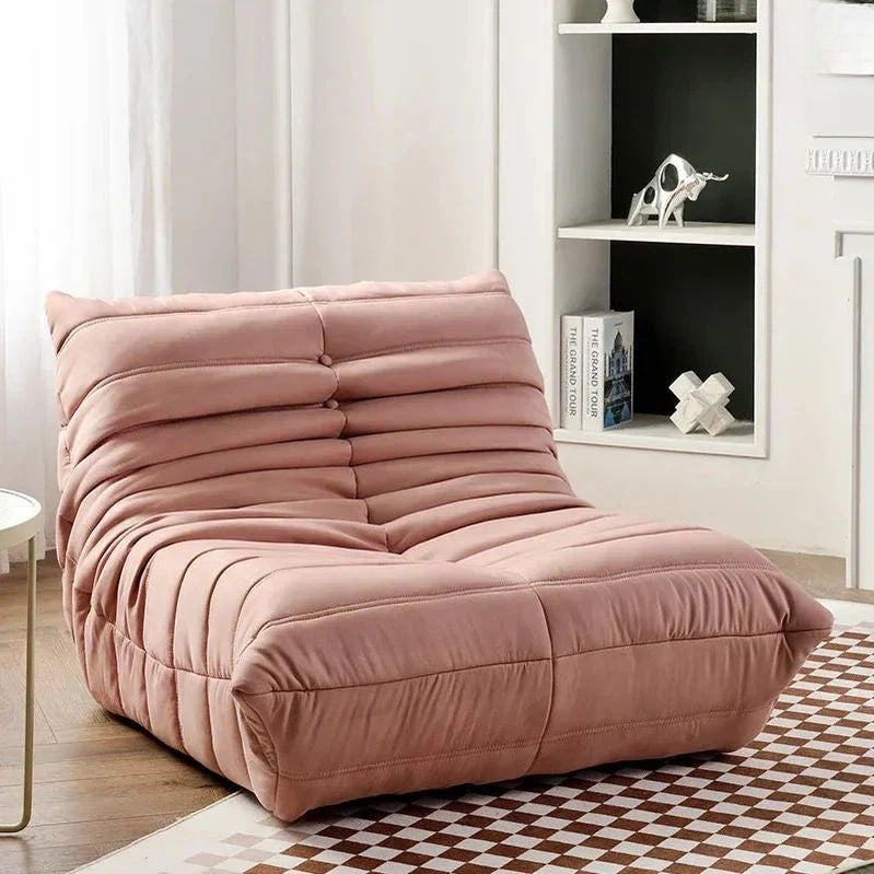 "Pink lounge chair in a room with a bookshelf and checkered floor."
