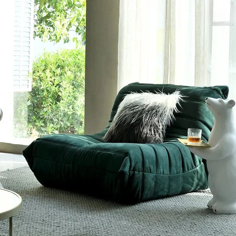 "Green bean bag chair with a fluffy pillow and a glass of beer in a room with large windows."