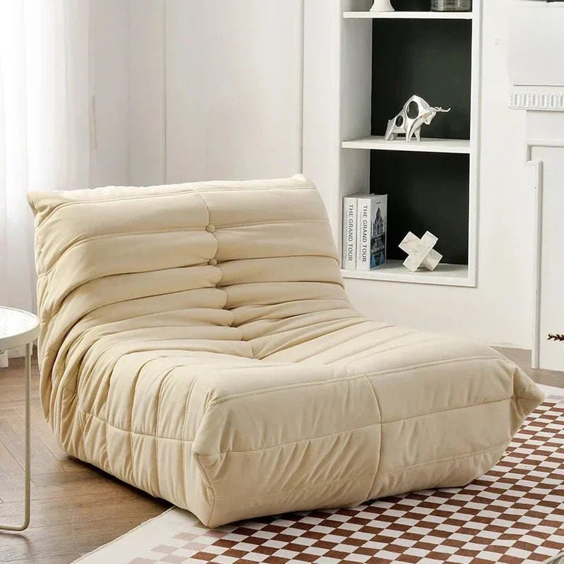 "Beige bean bag chair in a room with a bookshelf and checkered rug."