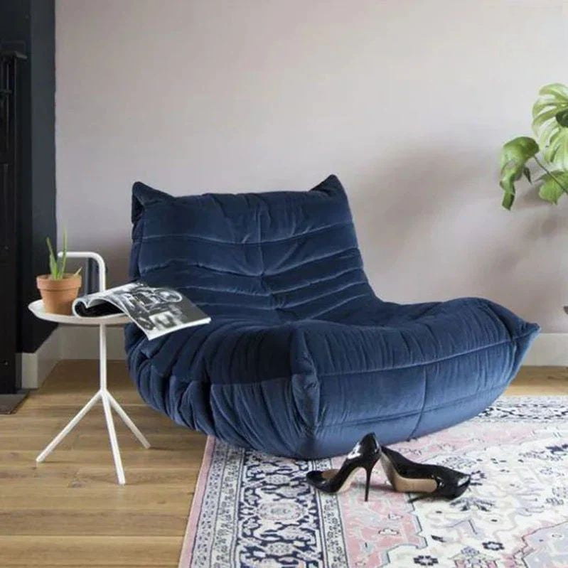 "Blue armchair in a room with a small table, shoes, and a plant."