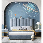 "Children's bedroom featuring a modern bed with a blue upholstered headboard, placed against a wall with a space-themed mural, including a planet and stars."
