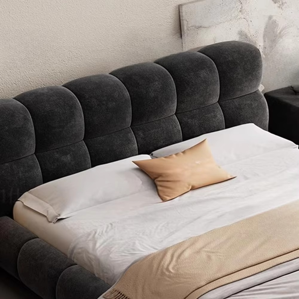 Gray upholstered headboard with a bed and beige pillow in a bedroom setting.