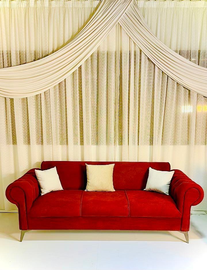 Red sofa with white cushions in front of a decorative curtain. Minimalist sofa design, Red crimson sofa style, Living room sofa. 