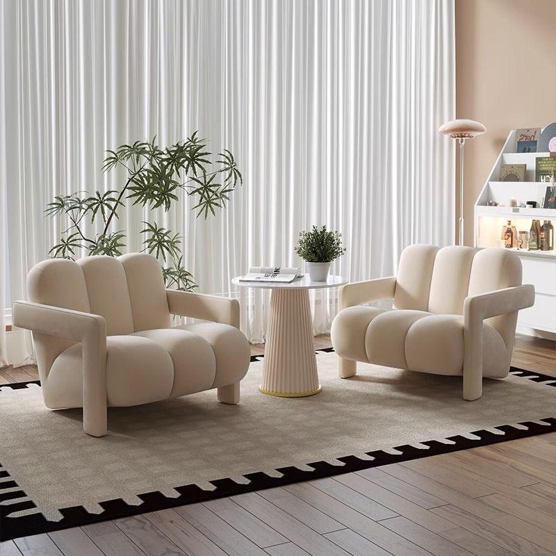 A beige velvet fabric Danish Scandinavian style single sofa chair with a unique design, placed in a room with a round side table and a plant in the background. Indoor furniture, Scandinavian chair design, living room chair, outdoor furniture, bedroom furniture. 