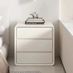 "A white minimalist Italian modern nightstand with three drawers, placed beside a bed in a simple bedroom setting. Bedside table, minimalist bedside design, bedroom furniture, wood furniture, modern nightstand. 