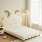 Children's bed with rabbit ear headboard in a room with a lamp and window.