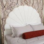 White shell-shaped headboard with pillows and a red cylindrical pillow against a patterned wall.