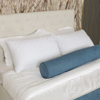 Blue cylindrical pillow on a bed with white pillows and beige headboard.