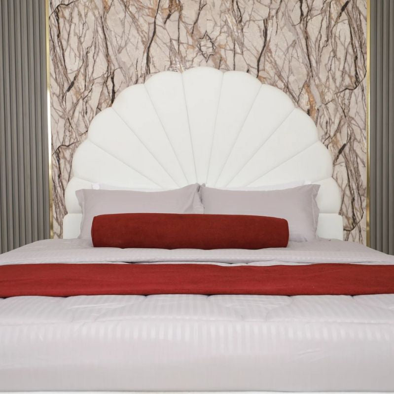 White upholstered headboard with red and gray pillows against a marble wall.