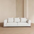 White sofa with three cushions against a beige wall with  vertical stripes.