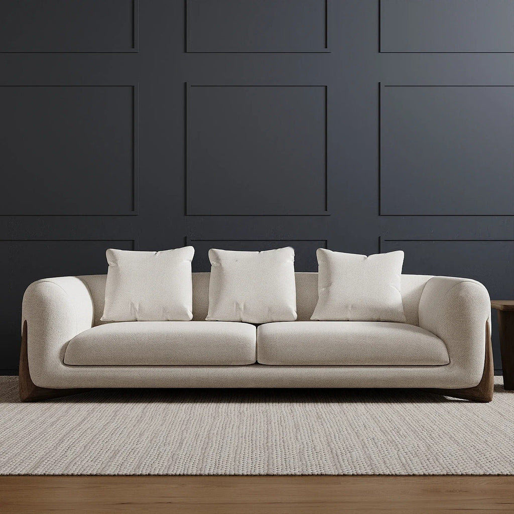 Beige sofa with white cushions against a dark paneled wall.