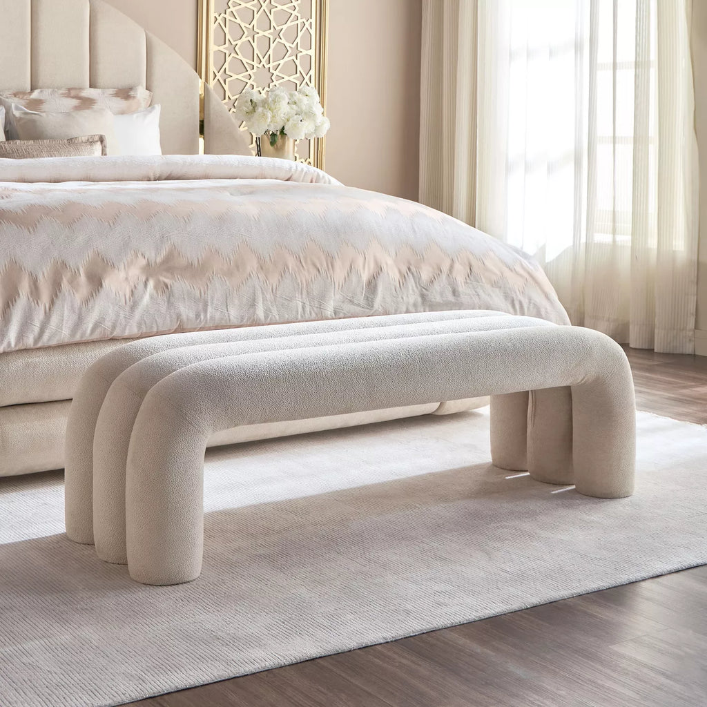 Beige upholstered bench in front of a bed with white bedding in a bedroom setting. Bench with storage, Bed accessories, Bedroom furniture. 