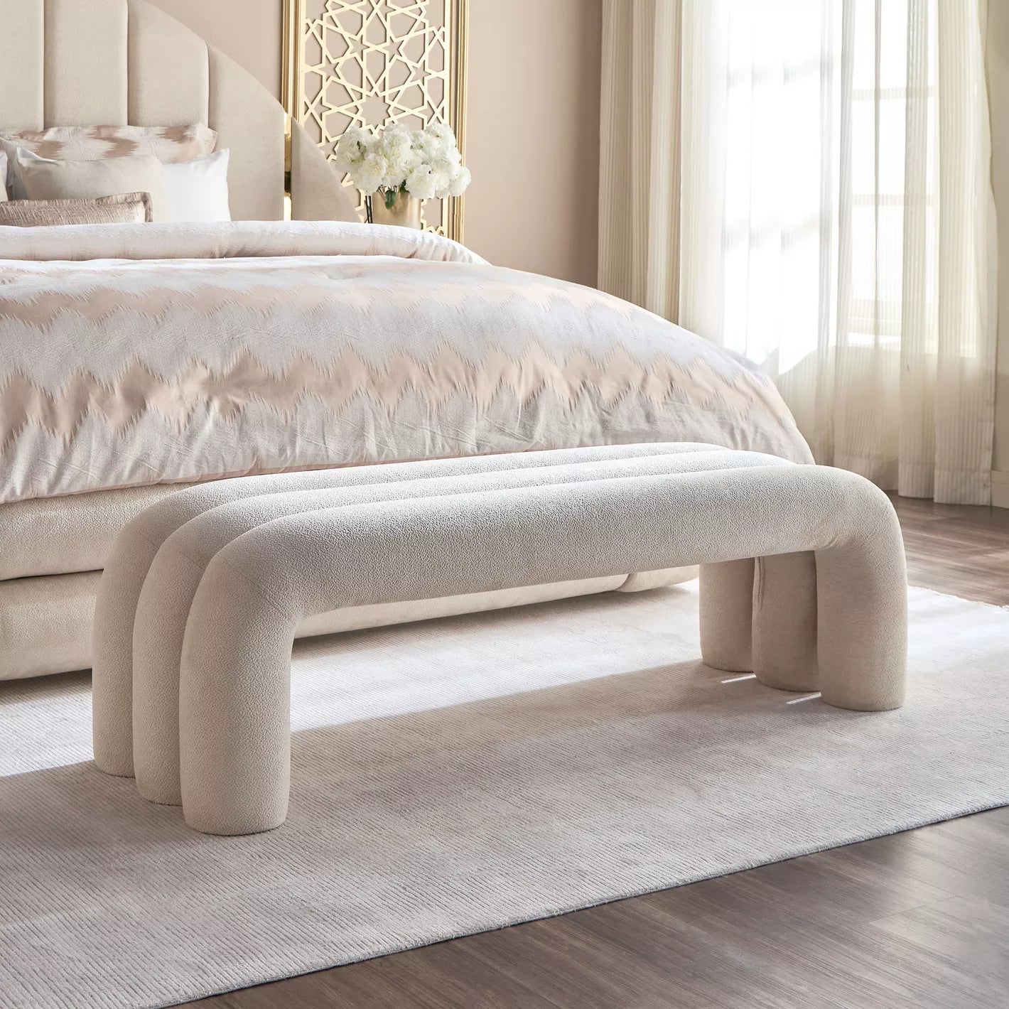 Beige upholstered bench in front of a bed with white bedding in a bedroom setting. Bench with storage, Bed accessories, Bedroom furniture. 