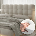 Beige upholstered headboard with a close-up of a hand on a white pillow.