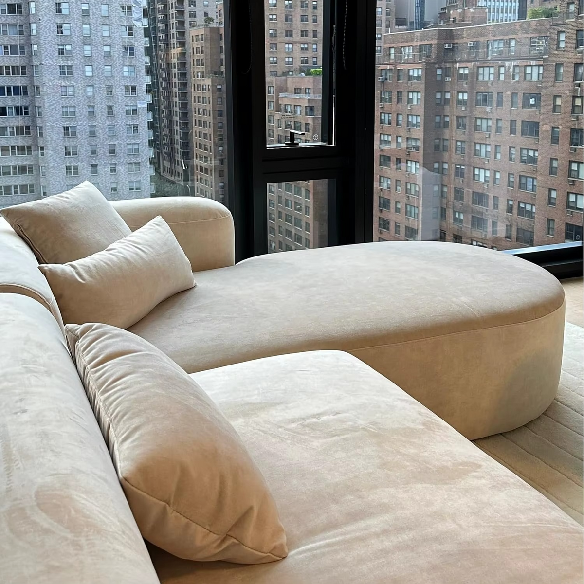 Beige sectional sofa in a room with large windows showing cityscape