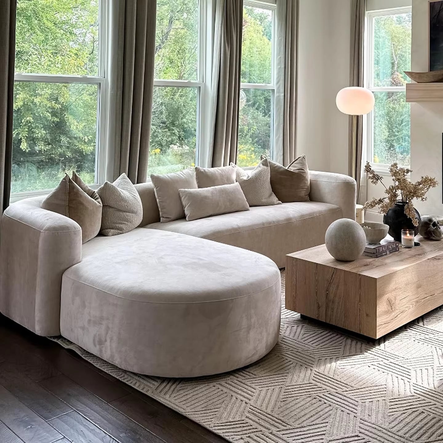 "Modern living room with a beige sectional sofa, round ottoman, and wooden coffee table."