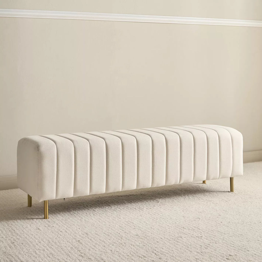 "Beige upholstered bench with gold legs on a neutral background"