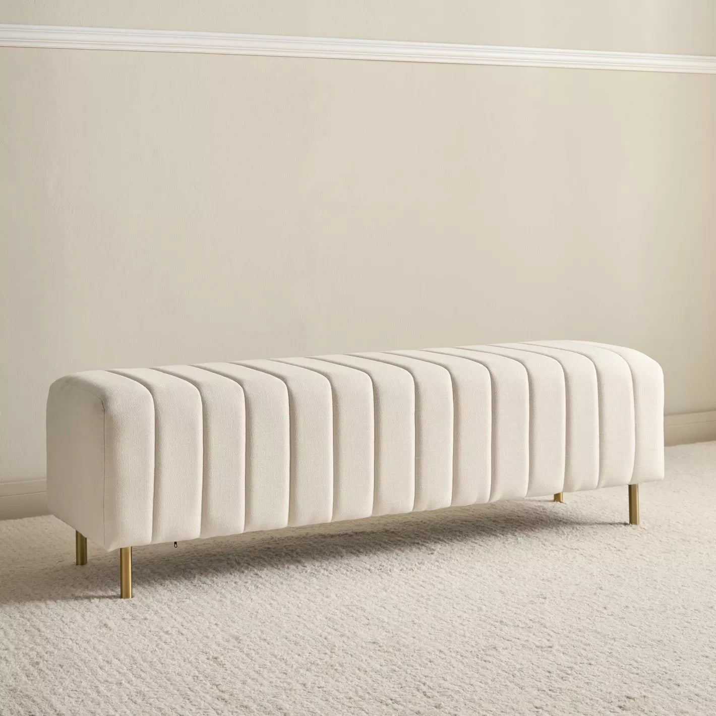 "Beige upholstered bench with gold legs on a neutral background"