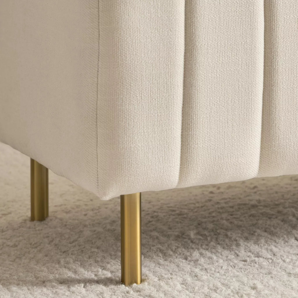 "Beige upholstered chair with gold legs on a textured surface"