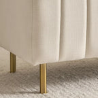 "Beige upholstered chair with gold legs on a textured surface"
