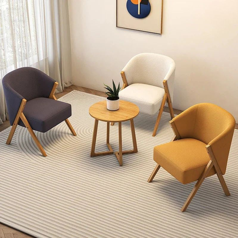 Three armchairs in different colors arranged around a small wooden table in a room with a rug and wall art.