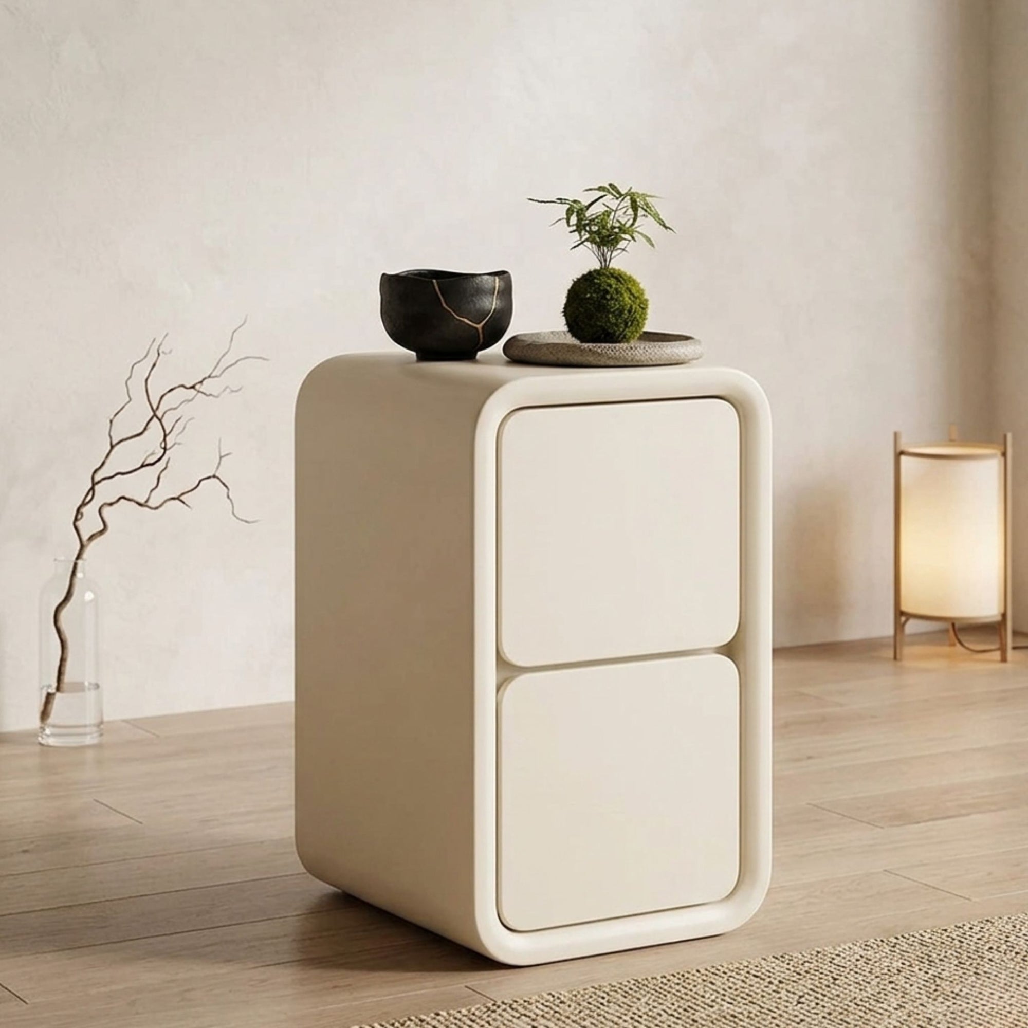 A lifestyle image of the Vellum Solace Tier Nightstand by Philips Modern Homes in a serene Japandi-inspired bedroom. The cream-toned, two-drawer nightstand is styled with a vintage alarm clock and gold vase, set against a warm textured wall and traditional shoji screen