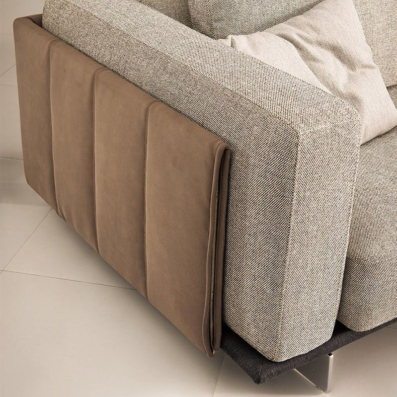 "Corner of a gray and brown sofa with textured cushions on a light tiled floor."
