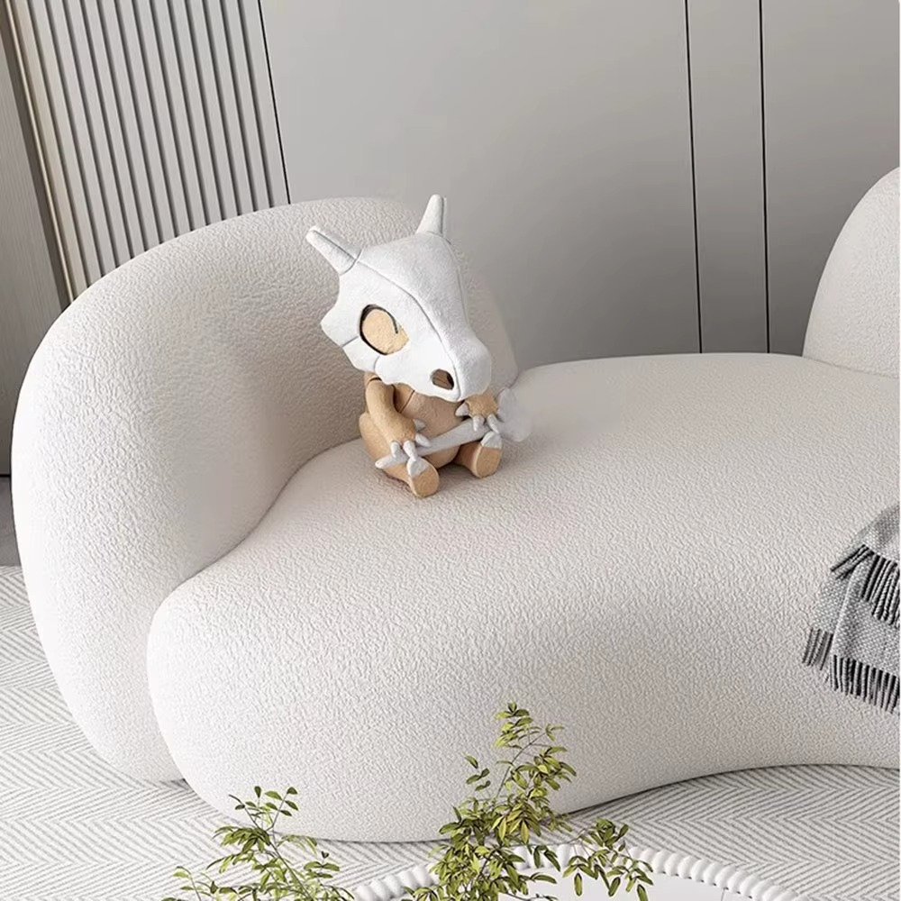 White plush toy with a skull design on a white cushion in a minimalistic room.