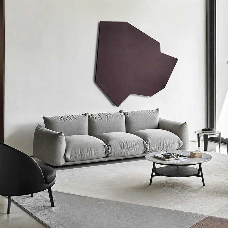 "Puffy European Style 3-Seater Sofa. Modern living room with a gray sofa, black chair, and geometric wall art."