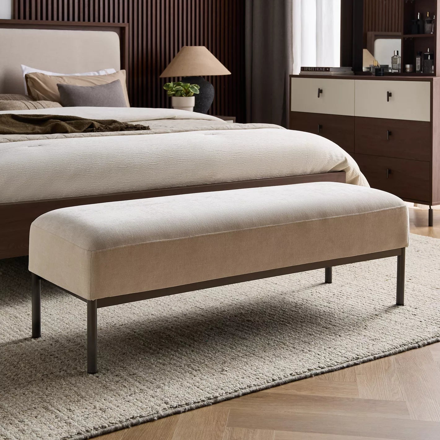 Beige upholstered bench in front of a bed in a bedroom setting. Bedroom accessories, Minimalist bench chair. 
