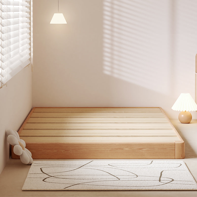 Wooden platform bed in a minimalistic room with light-colored walls and a rug.