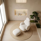 A full-scene view of the Velia white boucle rocking chair and ottoman in a serene, nature-inspired Japandi bedroom beside a large window, featuring natural materials, a bonsai tree, and a cast-iron tea set on a jute rug